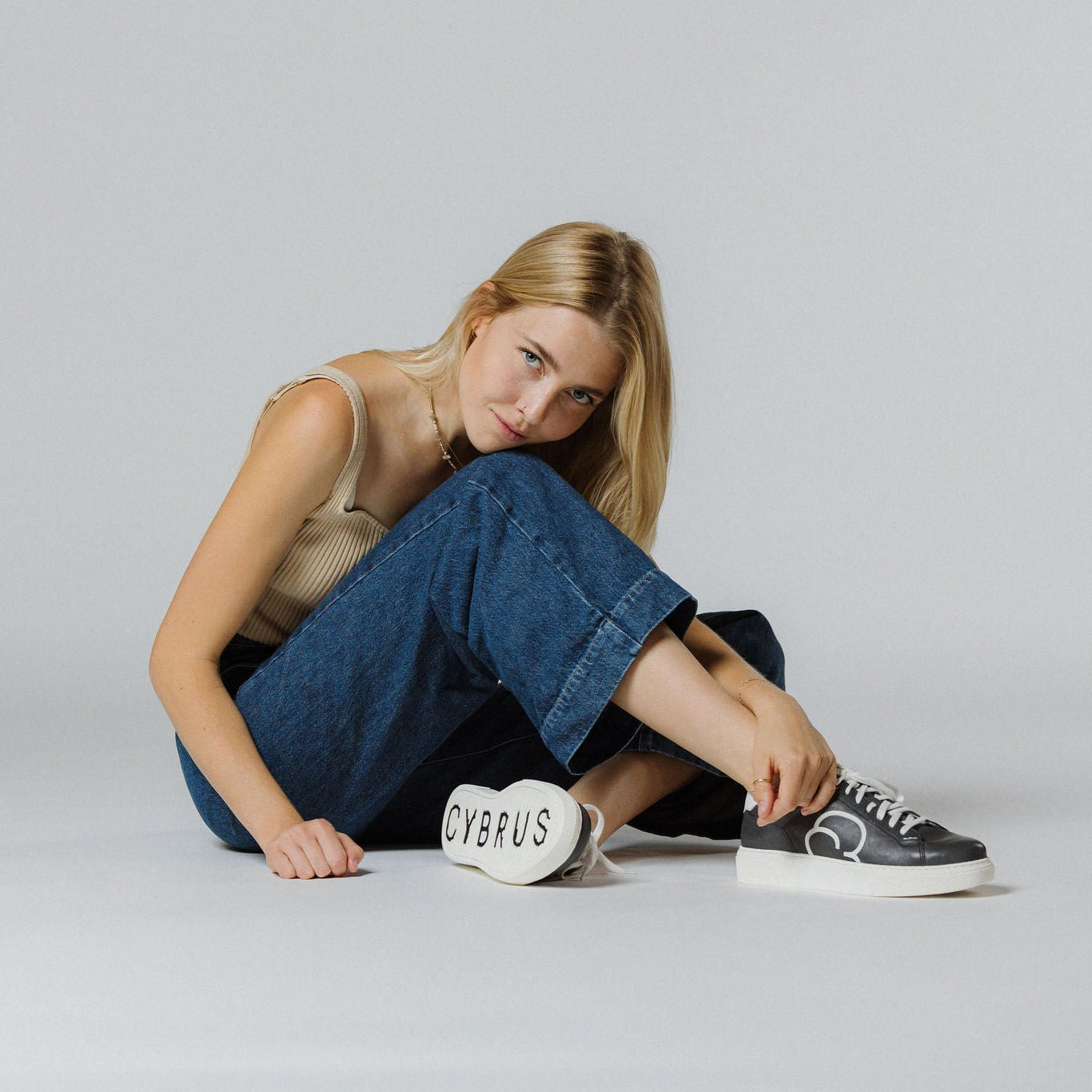 "Frau am Boden sitztend in blauen Jeans und dem CYBRUS Sneaker 49er dunkelblau weiss"