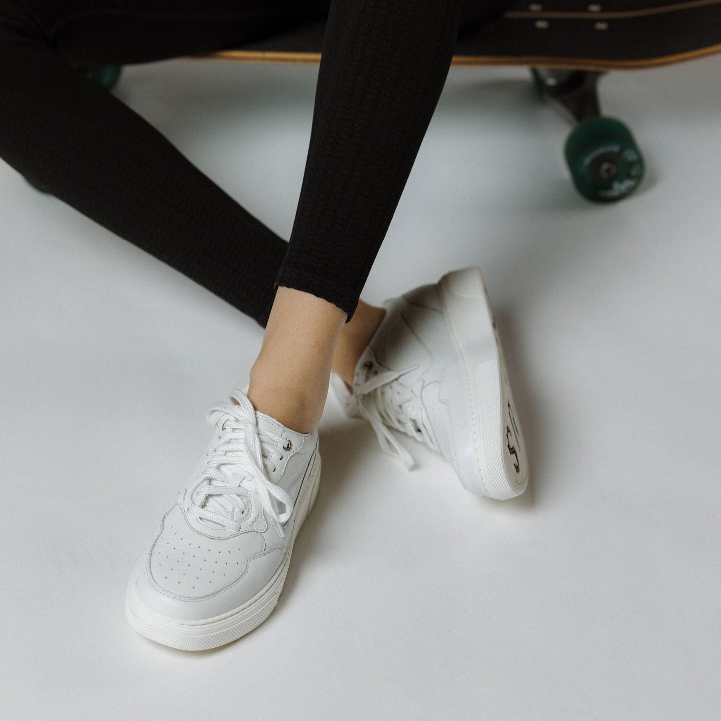 "Frau auf Skateboard sitztend in schwarzen Hosen und dem CYBRUS Sneaker HAULA weiss"