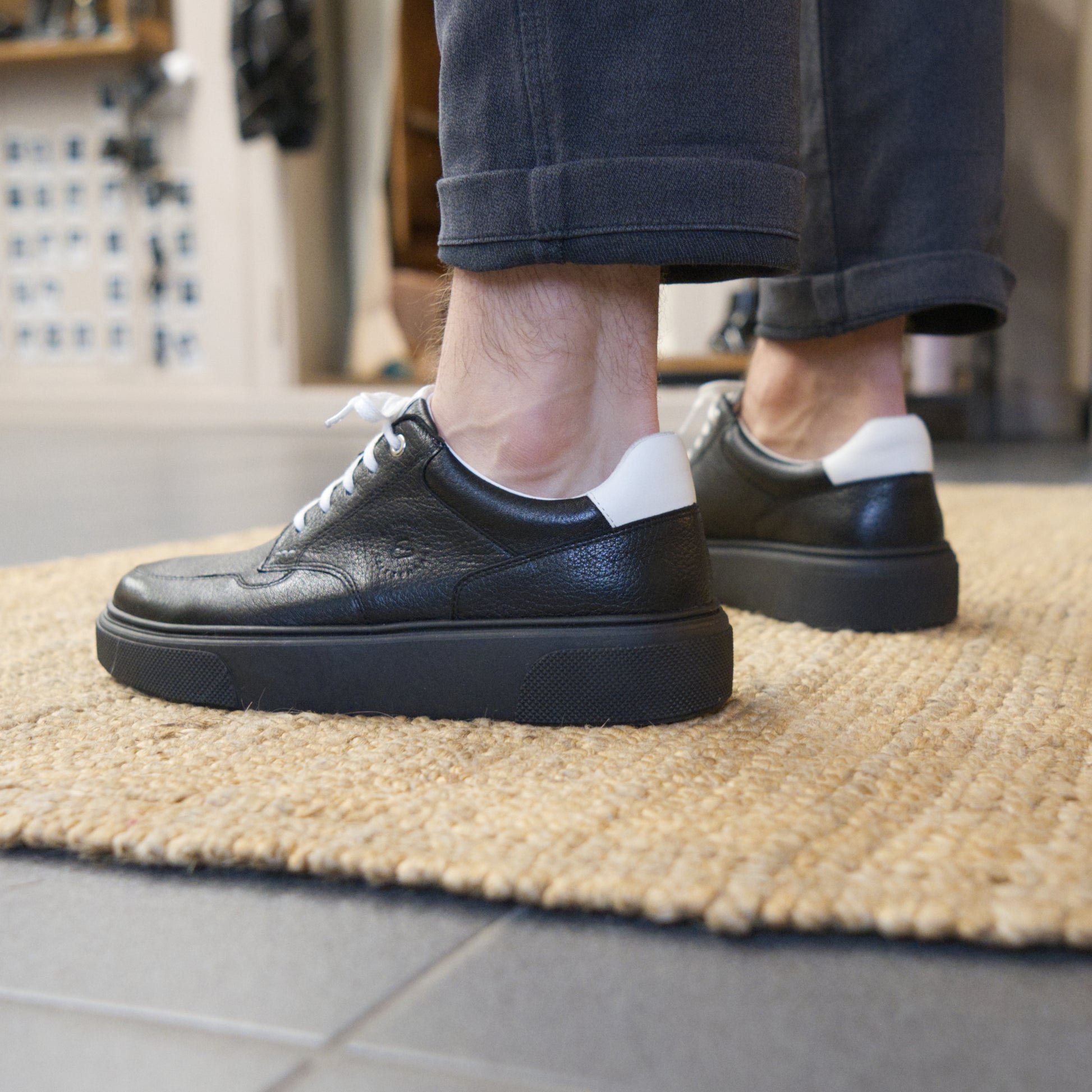 Männerfüsse mit CYBRUS Sneaker Nold schwarz auf hellbraunem Teppich. 